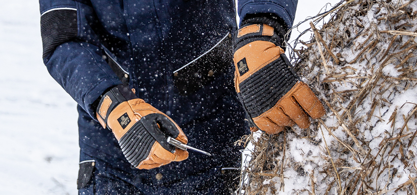 Person wearing waterproof insulated work gloves  spreads hay on a snowy ranch.