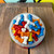 A bowl of vibrant bone-shaped candies displayed on a wooden table with a colorful background — casual and fun presentation.