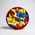 A close-up of colorful bone-shaped candies in a red bowl — bright blue, yellow, orange, and white pieces with a glossy finish.