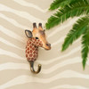 Three quater view of a hand-carved wooden Giraffe wall hook, mounted on striped wall.