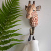 Three quater view of a hand-carved wooden Giraffe wall hook, mounted on striped wall, carrying a kitchen towel.