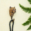 A hand-carved Leopard wall hook mounted on a wall, holding a black beads necklace against a light yellow background.