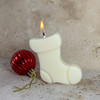Lit soy wax Christmas stocking shaped candle next to a red ornament.