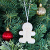 Christmas gingerbread man and hanging next to two ornaments on a green Christmas tree.