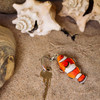 Clownfish wooden keychain and key among seashells and sand, highlighting the wildlife and nature theme.