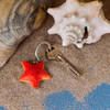 Hand-painted orange Starfish wooden keyring close-up on beach sand next to a key and large seashell