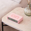 Pink Lexon Flip Alarm Clock (ON side up) sitting on a marble bedside table next to a vase in a modern bedroom setting.