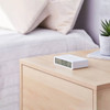 White Lexon Flip Alarm Clock on a light wood bedside table, blending into a simple, Scandinavian-style bedroom.