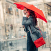 Woman using BLUNT Metro Cherry Red umbrella on city street – side profile.