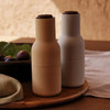 Warm tabletop scene featuring AUDO Barley bottle grinders with walnut lids on a wooden platter.