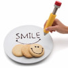 Hand decorating a cookie on a plate with a smiley face using the silicone cake decorating pen.