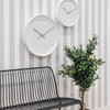 Two Karlsson Mr. White Numbers wall clocks on a striped hallway wall above a bench.