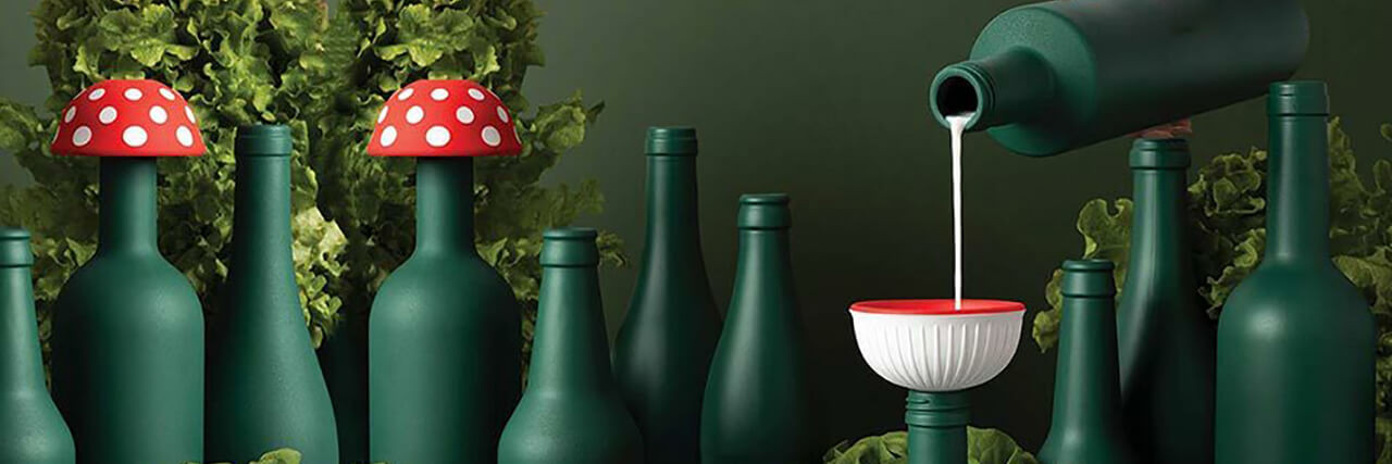 A person pours a white liquid into green bottles adorned with silicone funnels resembling mushrooms.