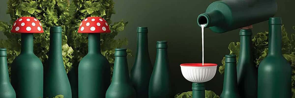 A person pours a white liquid into green bottles adorned with silicone funnels resembling mushrooms.