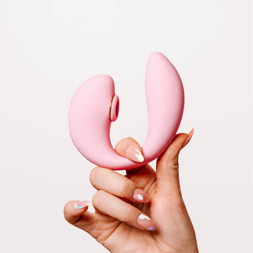 A woman's hand holding the pink Tiff dual-action vibrator, highlighting its ergonomic C-shape for G-Spot and clitoral stimulation. A woman's hand holding the pink Tiff dual-action vibrator, highlighting its ergonomic C-shape for G-Spot and clitoral stimulation.