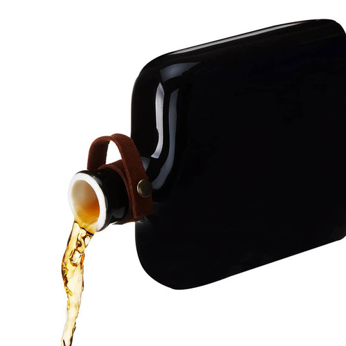 Viski Nautilus black ceramic hip flask pouring amber whisky liqueur with a natural cork stopper and genuine leather strap on a white background.