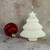 Lit soy wax Christmas tree shaped candle with a star topper next to a red ornament.