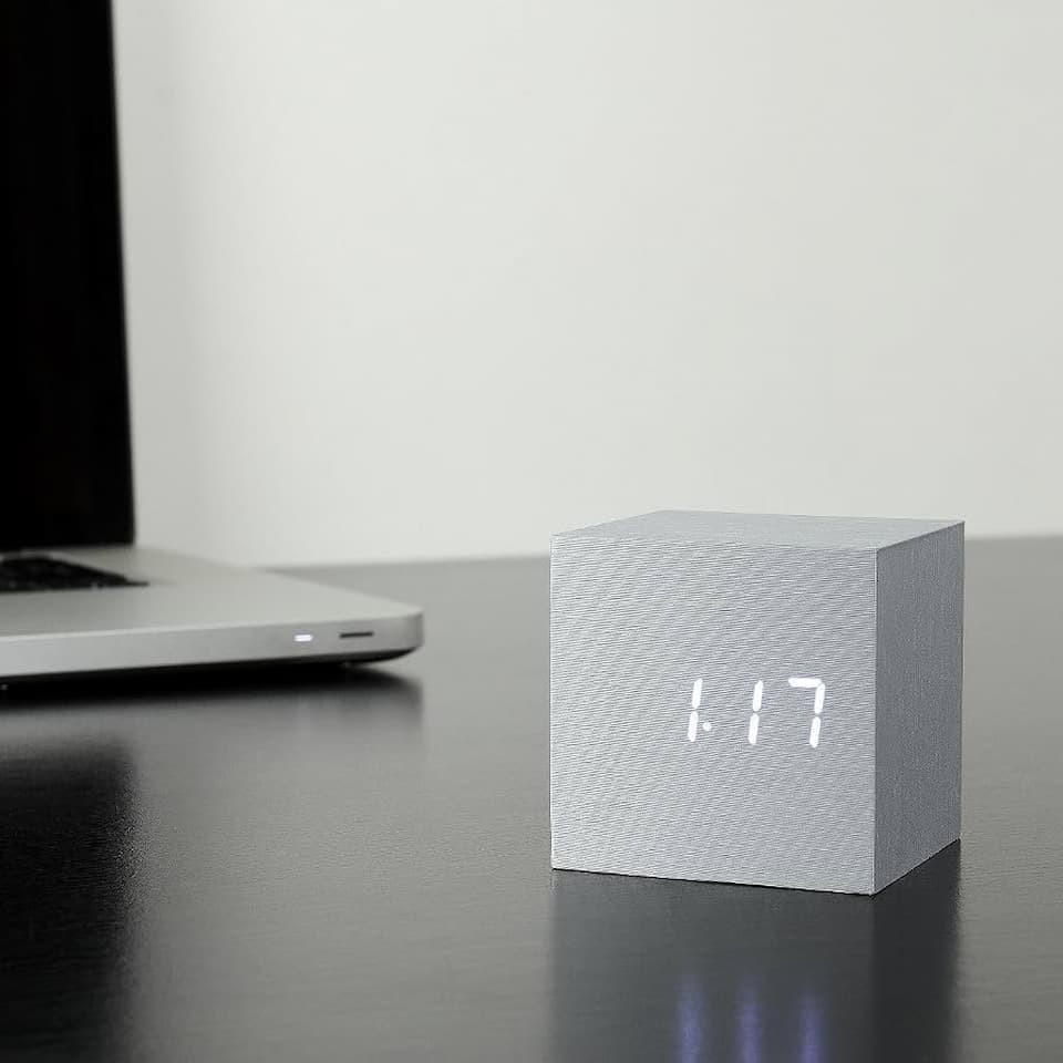 Gingko Cube Click Clock in brushed aluminium sitting on a dark desk next to a laptop displaying 1:17 in glowing white LED.