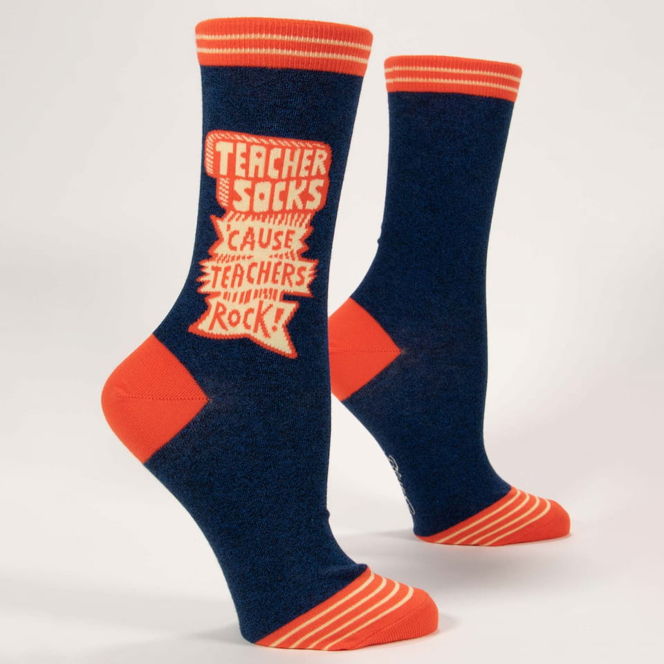 Pair of dark blue women's crew socks with orange heels, toes, striped cuffs, and text reading Teacher Socks 'Cause Teachers Rock! standing upright.