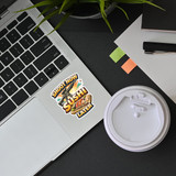 Shoot Now Sushi Later sticker applied on laptop beside coffee cup in workspace setting