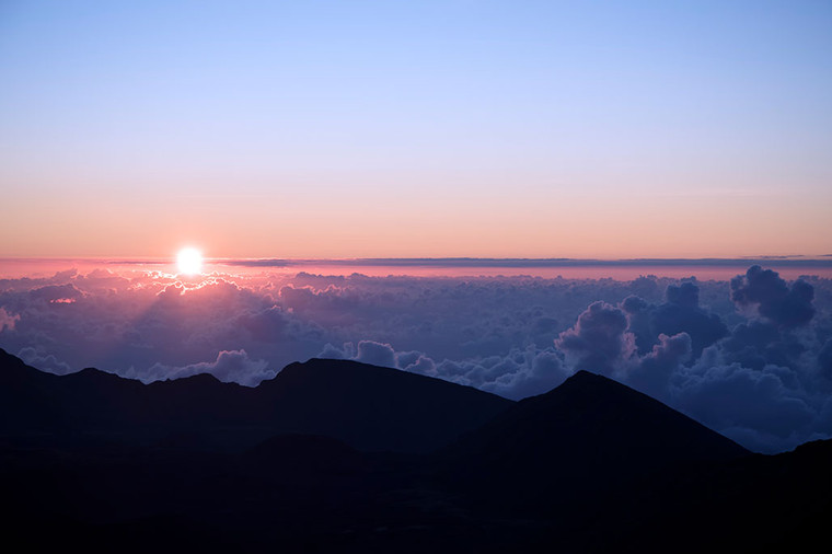 Sunrise over the Haleakala crater in Maui, Hawaii, with pink, blue, and purple hues filling the sky.
