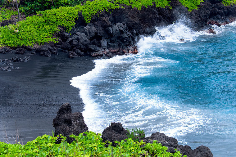 Aerial view of the contrasting black sand beach and turquoise waves at Waianapanapa State Park in Maui, Hawaii.