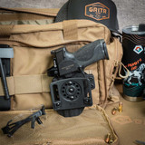 Inside the open GRITR range bag, a OMNI IWB/OWB Ambidextrous Kydex Holster rests beside GRITR Goggles and a Titanium Mug