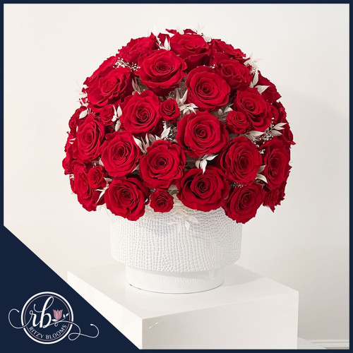 Luxurious preserved red roses arranged in a dome shape with white foliage accents, displayed in a textured white hat box by Ritzy Blooms. Hand Crafted in Fort Lauderdale
