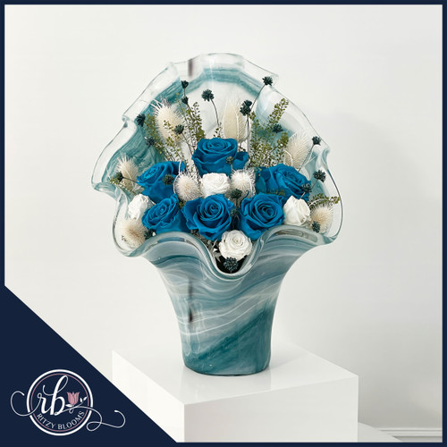 Ocean-inspired preserved flower arrangement featuring vibrant blue and white roses in a wavy glass vase. Elegant home and office decor by Ritzy Blooms. Crafted in Fort Lauderdale