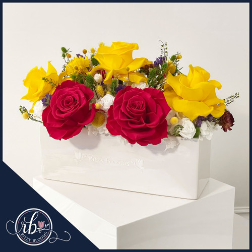 Vibrant preserved floral arrangement featuring hot pink and yellow roses with white accents and greenery, elegantly displayed in a white ceramic vase by Ritzy Blooms in Fort Lauderdale.