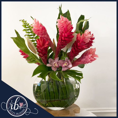 Tropical flower arrangement with red and pink ginger flowers, cymbidium orchids, and tropical greenery in a moon-shaped oval flat glass vase, designed by Ritzy Blooms in Fort Lauderdale.