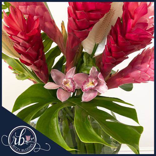Tropical flower arrangement with red and pink ginger flowers, cymbidium orchids, and tropical greenery in a moon-shaped oval flat glass vase, designed by Ritzy Blooms in Fort Lauderdale.