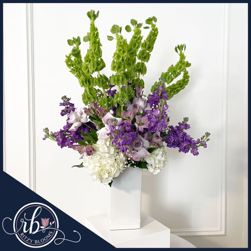 Fresh flower arrangement with lavender roses, purple stock, lavender alstroemerias, Bells of Ireland, and white hydrangeas in a white vase