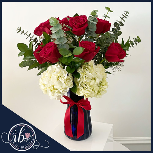 12 red roses and white hydrangeas arrangement in a deep blue vase with greenery and satin ribbon, available for same-day delivery in Fort Lauderdale.