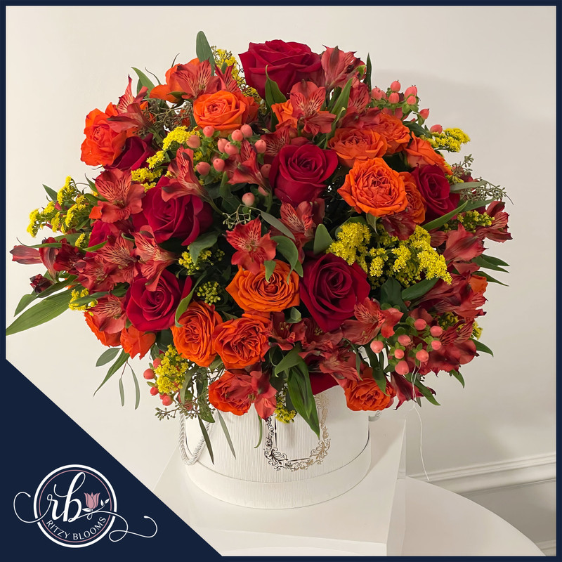 a striking floral arrangement from Ritzy Blooms' Fall Collection. This bouquet features a rich blend of deep red and fiery orange roses, vibrant alstroemeria, soft yellow solidago, and pink hypericum berries, all beautifully arranged to capture the warm glow of autumn. Crafted by Ritzy Blooms in Fort Lauderdale
