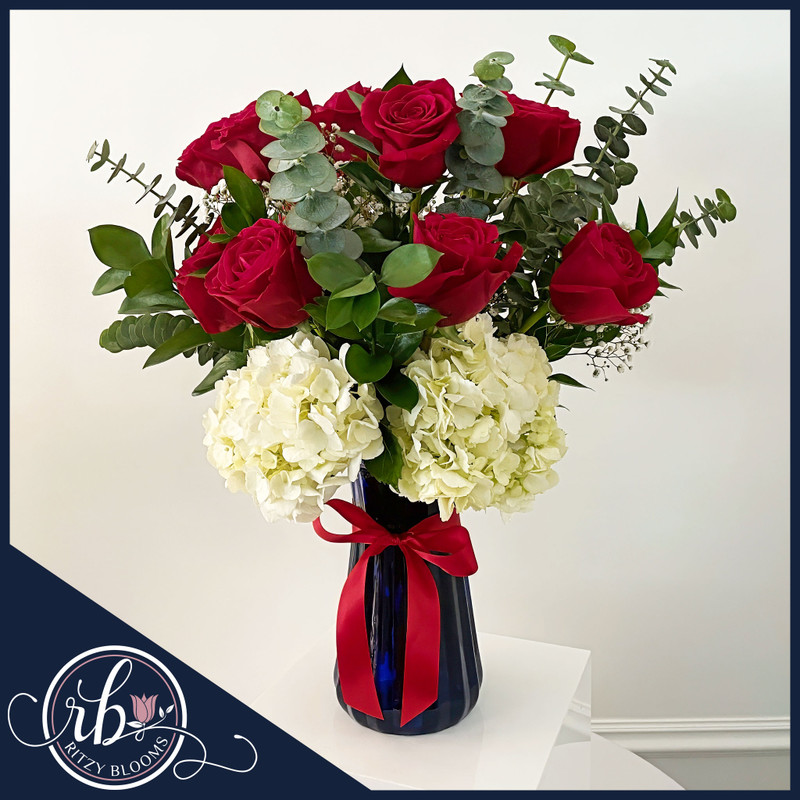 12 red roses and white hydrangeas arrangement in a deep blue vase with greenery and satin ribbon, available for same-day delivery in Fort Lauderdale.