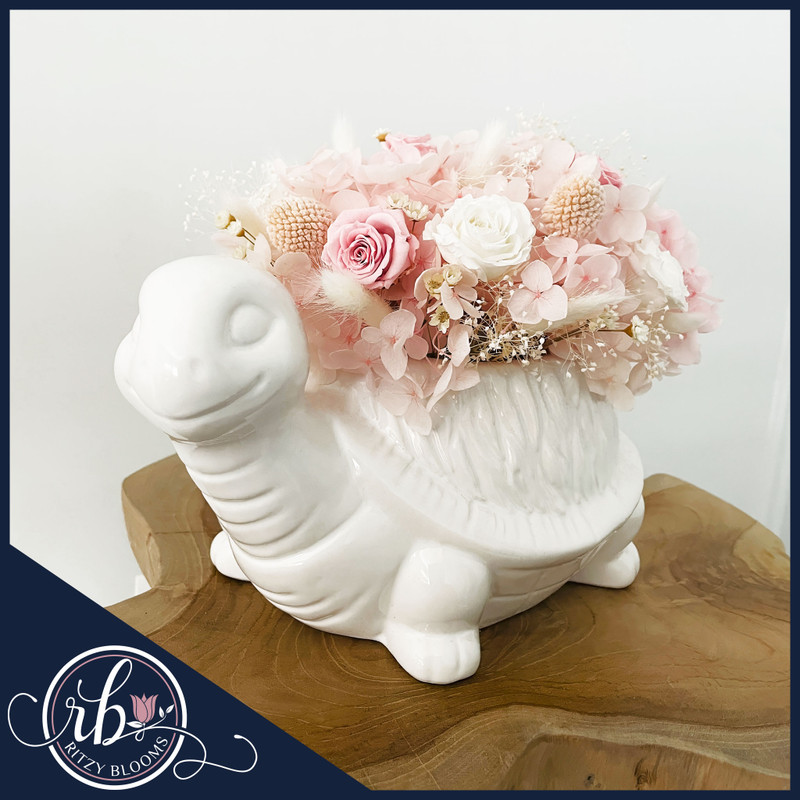 Petite blush preserved flower arrangement in a white ceramic turtle vase, handcrafted by a Fort Lauderdale florist for bedroom and nursery decor.