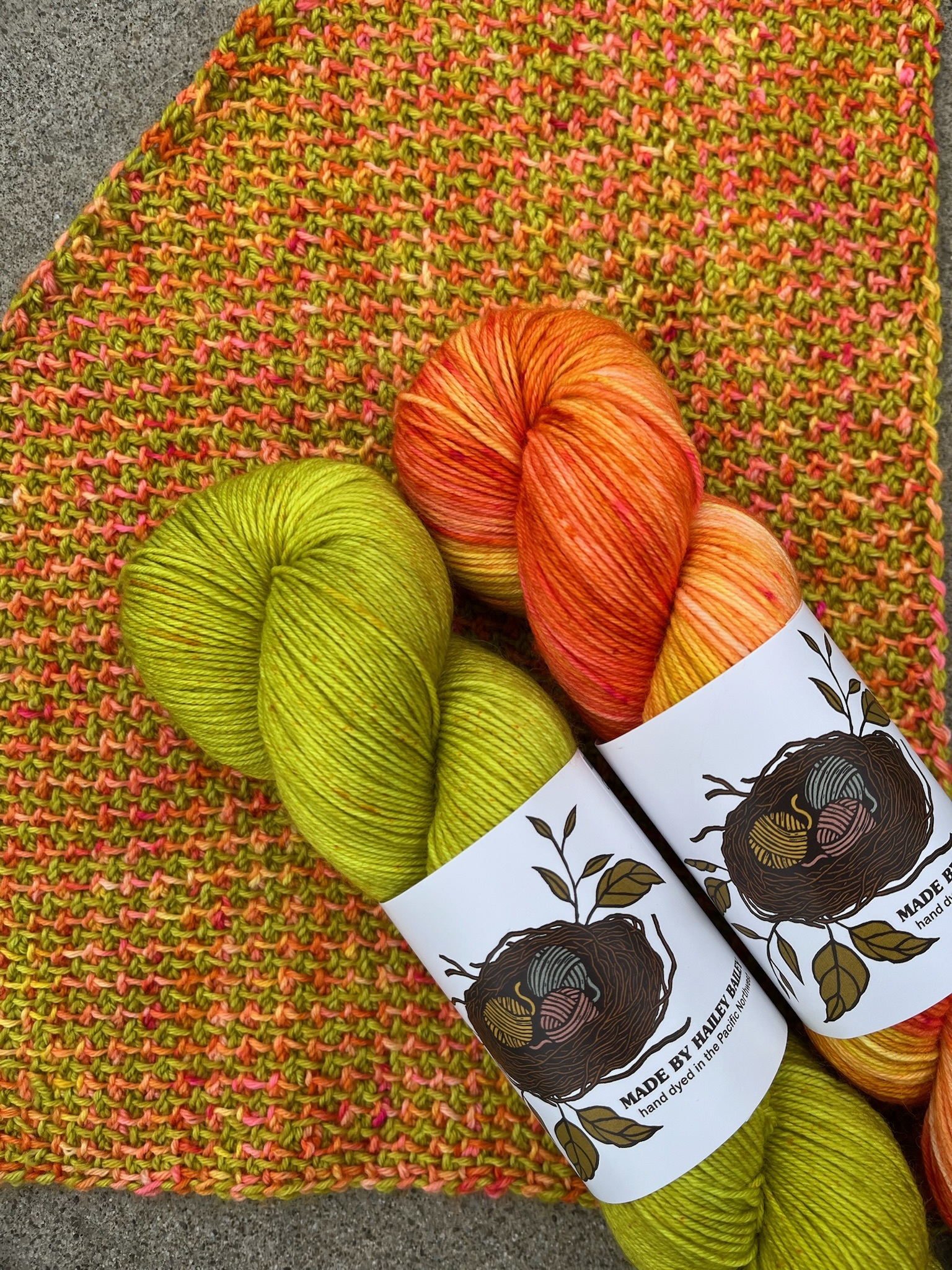 Two skeins of Made by Hailey Bailey yarn, in custom colorways Sprout and Flourish, shown with a sample made with these colorways