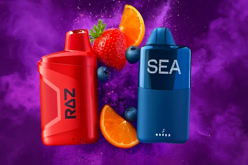 The photo features two colorful vape devices set against a vibrant purple smoky background. The red device on the left is labeled “RAZ,” while the blue one on the right is marked “SEA.” Fresh fruits, including strawberries, blueberries, and orange slices, surround the devices, highlighting the fruity flavors they represent.