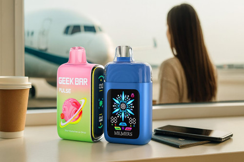 Two disposable vapes, a pink Geek Bar Pulse and a blue Memers device, are placed on an airport terminal ledge next to a coffee cup, smartphone, and passport. In the blurred background, a passenger looks out the window at a large airplane parked on the tarmac.