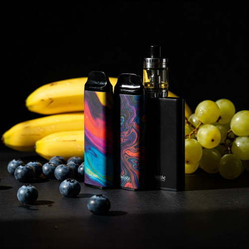 The image shows a sleek vape device standing upright on a white surface. The vape device is black with metallic accents and has an elegant, modern design. Surrounding the vape device are several small decorative elements, including white and gold pebbles, adding a touch of sophistication to the composition. The background is softly lit, creating a clean and minimalist aesthetic that highlights the vape device as the focal point of the image. The overall scene exudes a sense of elegance and luxury.