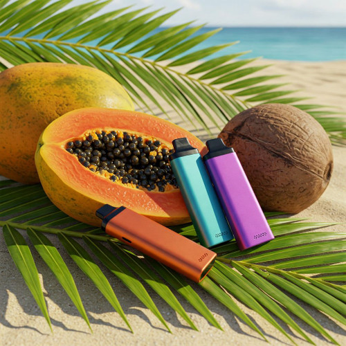 The image shows a tropical beach scene featuring three colorful vape devices placed on a bed of palm leaves. There is a halved papaya with black seeds, a whole papaya, and a whole coconut positioned in the background. The vape devices are in vibrant orange, blue, and purple colors. The backdrop includes a sandy beach with the ocean and sky in the background, creating a visually appealing composition that combines the tropical fruits and the lively colors of the vape devices.