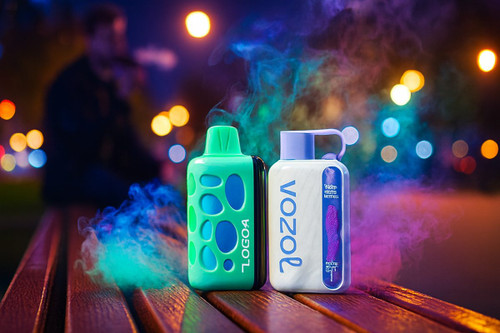 Two disposable vapes, one bright green with a textured pebble pattern and one white with blue branding, stand on a wooden park bench at night. Swirls of vibrant neon blue and purple smoke rise from the devices, illuminated by the warm glow of distant city bokeh lights. The cinematic shot captures the modern aesthetic of the vapes against a soft, dark background where a person is faintly visible in the distance.