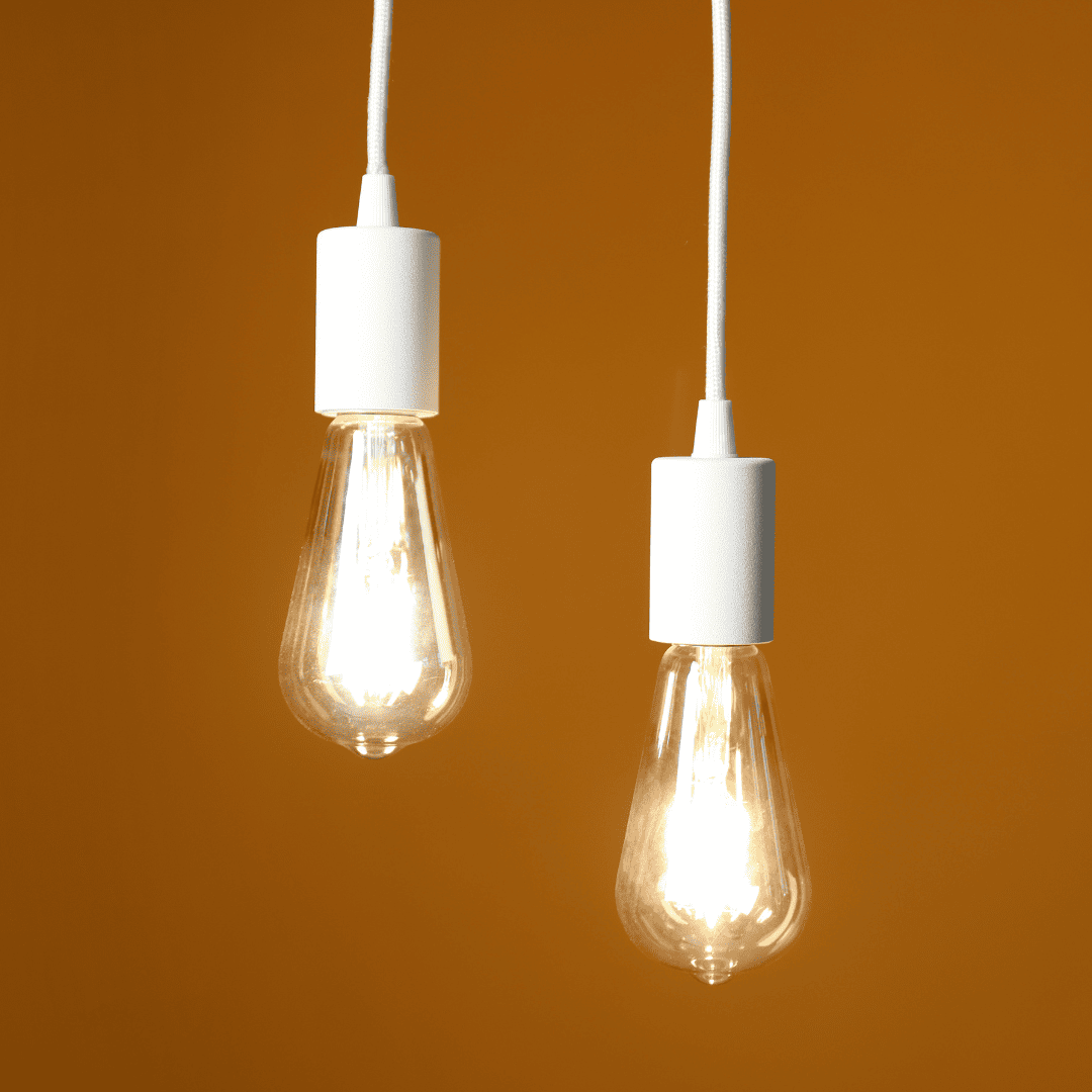Two illuminated vintage-style light bulbs hanging against warm orange background