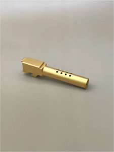 Gold TiN 9mm pistol barrel shown at an angle on a light background, highlighting its ported design and extended profile.


Angled view of a Gold TiN ported Glock 19 Gen 1-5 barrel on a light surface.
