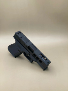 Angled view of the Kineti-Tech LWP Complete Slide for Glock® 19 Gen 5/19X in Armor Black CERAKOTE® finish. Features lightening window cuts for weight reduction, large port for gas venting, and RMSc optic cut for micro red dot compatibility.

Armor Black Kineti-Tech LWP Slide for Glock 19 Gen 5/19X with lightening cuts, ported design, and RMSc optic cut.