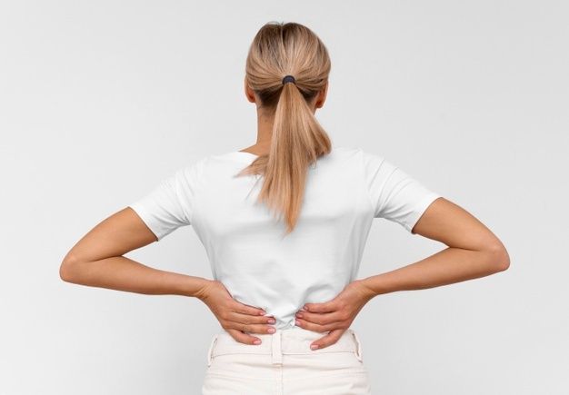 Woman dressed in white trying to soothe her painful back.