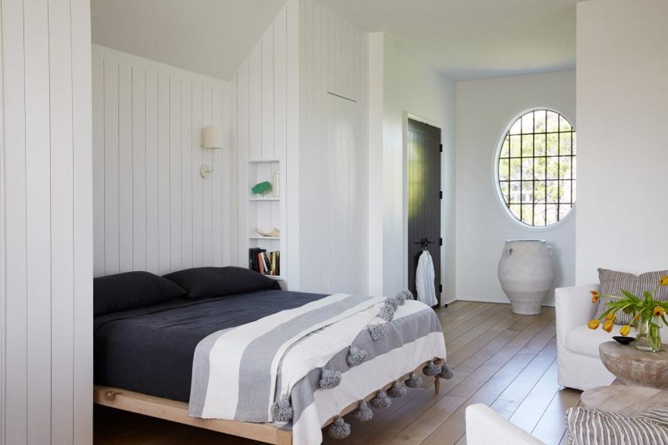 Master bedroom suite at Harrison Residence featuring white timber panel walls, hardwood floors and circular window — contemporary Hamptons style architecture Australia by Jeffrey Dungan Architects