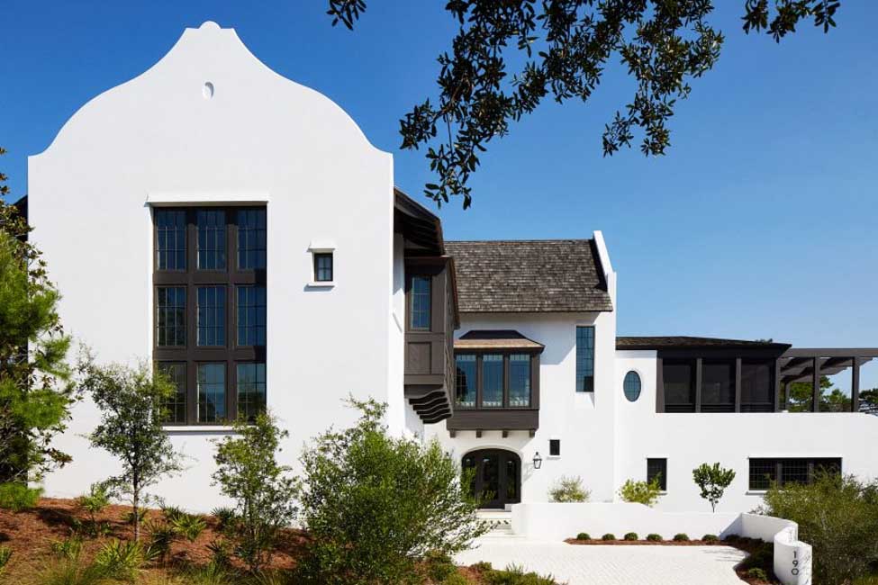 Harrison Residence exterior showcasing Hamptons style architecture Australia with crisp white stucco facade, black window accents and lush pine surrounds by Jeffrey Dungan Architects