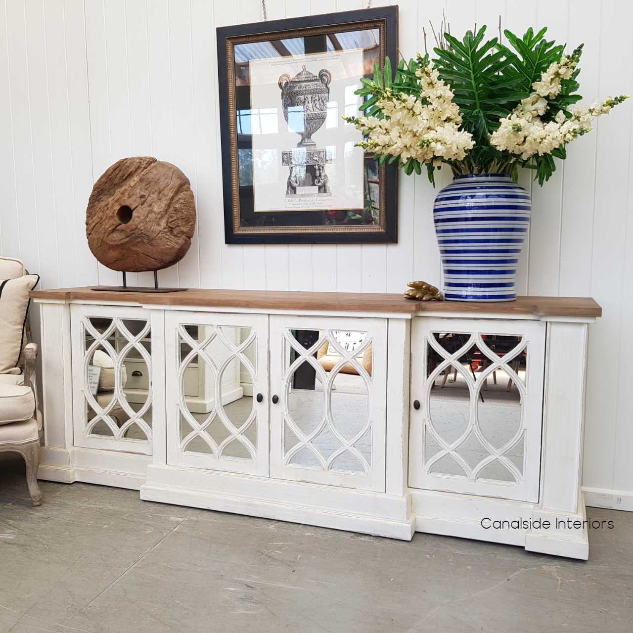 The Marielle Sideboard in a bright living room, highlighting the reflective beauty of its mirrored doors and the texture of its distressed stone finish.
